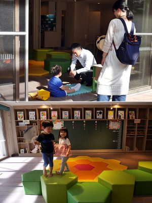 <上>保育園から帰ってすぐに、中庭からキッズスペースに立ち寄った男の子。中央の男性が萬富の仲渡孝雄さん。子どもたちや親御さんから「なかとさん、なかとさん」と呼ばれ親しまれている<br>
<下>広々としたキッズスペースで走り回って遊ぶ子どもたち