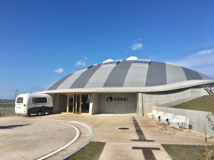 ▲山形県産のスギやカラマツを使ったドーム状の大屋根が特徴の『キッズドームソライ』は2018年11月にグランドオープン予定。ドーム内には地元ベンチャー『スパイバー』が運営する保育施設も併設され、サイエンスパーク内の企業の従業員の子どもたちを中心に保育対応予定となっている