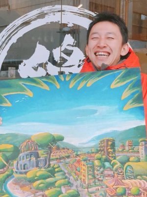 代表の正垣氏。抱えている絵は、「田舎と都会を融合した町をつくりたい」というビジョンから生まれた作品だ。象徴として、都会の広島市でも田舎と同じように緑がたくさん茂っている。原爆投下からちょうど100年になる2045年の実現を目指している