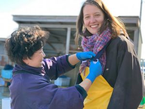 八雲町の春の風物詩、ホタテの耳吊り作業(養殖用のロープにホタテの稚貝を取り付ける)体験をするため、作業着に着替える外国人ゲスト