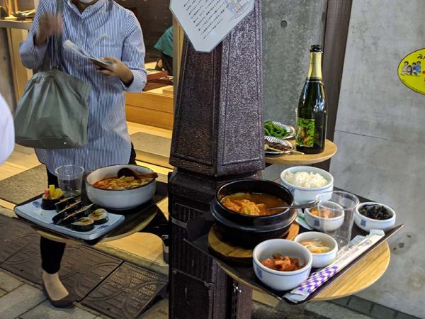 写真のような韓国料理のほか多様な食事が楽しめる。器は飲食店のもののほか使い捨ての簡易容器を使用するケースも。飲み物のテイクアウトや持ち込みも自由(アーツアンドスナック運動実行委員会)