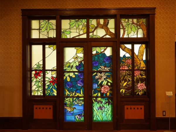 貞奴と桃介が多くの客を迎えた大広間。新築で復元したところだが、写真左奥の円形ソファーとその後ろの上げ下げ窓は創建当初のもの。売却されたあとに解体されたが他の部屋に転用されていて残ったという。ソファーは修繕するときに内部から見つかった布切れを基に伝統工芸士に依頼して新調し、当時に似た雰囲気になっている。円形ソファーは、深く腰をかけると沈むようにゆったりとした座り心地だが、座面の先端に板が入っているので、浅く腰をかけるとシャキッと背筋が伸びるようだ。緒方館長いわく「当時はお着物を着られていたので気崩れないですよね」とのこと