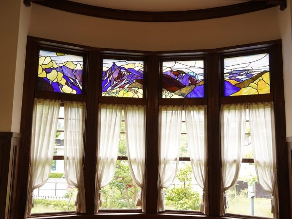 貞奴と桃介が多くの客を迎えた大広間。新築で復元したところだが、写真左奥の円形ソファーとその後ろの上げ下げ窓は創建当初のもの。売却されたあとに解体されたが他の部屋に転用されていて残ったという。ソファーは修繕するときに内部から見つかった布切れを基に伝統工芸士に依頼して新調し、当時に似た雰囲気になっている。円形ソファーは、深く腰をかけると沈むようにゆったりとした座り心地だが、座面の先端に板が入っているので、浅く腰をかけるとシャキッと背筋が伸びるようだ。緒方館長いわく「当時はお着物を着られていたので気崩れないですよね」とのこと