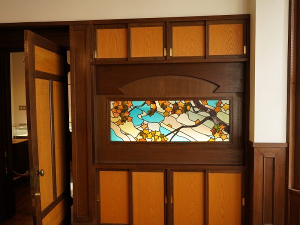 貞奴と桃介が多くの客を迎えた大広間。新築で復元したところだが、写真左奥の円形ソファーとその後ろの上げ下げ窓は創建当初のもの。売却されたあとに解体されたが他の部屋に転用されていて残ったという。ソファーは修繕するときに内部から見つかった布切れを基に伝統工芸士に依頼して新調し、当時に似た雰囲気になっている。円形ソファーは、深く腰をかけると沈むようにゆったりとした座り心地だが、座面の先端に板が入っているので、浅く腰をかけるとシャキッと背筋が伸びるようだ。緒方館長いわく「当時はお着物を着られていたので気崩れないですよね」とのこと