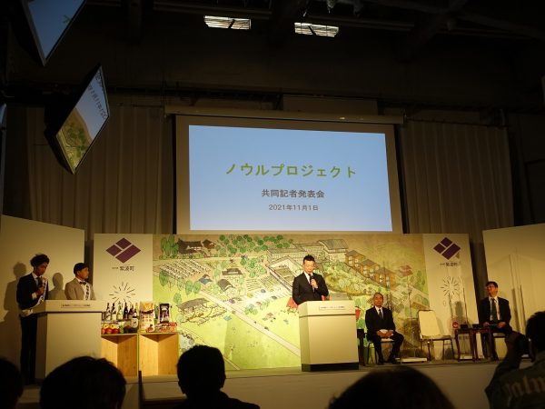 事業プレゼンを行う岡崎氏の後ろには、「吉本・オガール地方創生アカデミー」の全体構想を表したイラストボードが。約15,000平米の長岡小学校跡地にさまざまな事業イメージが描かれている