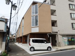 細長い三角形の土地に建つ六角橋の四軒長屋。茶色の細長い建物である