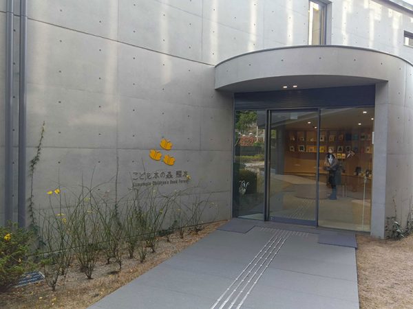 蝶を施したロゴマークの横に立つのは施設の案内をしていただいた「こども本の森 熊本」の主任主事・坂口沙采さん