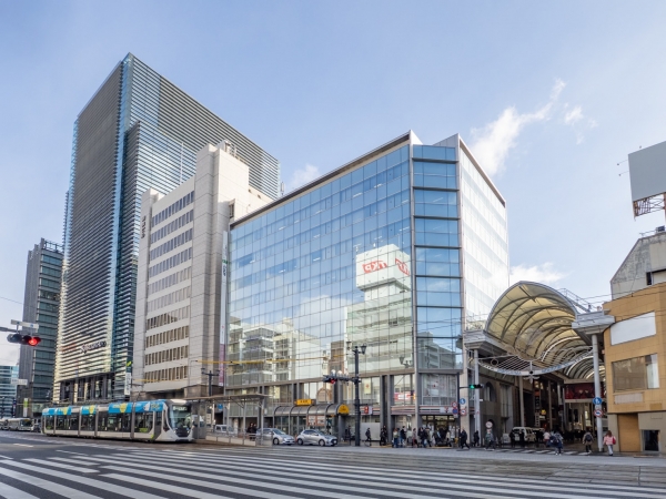 本通交差点から見た本通商店街の再開発対象エリア北側の様子。手前のガラス張り建物が「明治安田生命広島本通ビル」、その左側の灰色の建物が銀泉広島ビル」(2025年12月撮影)