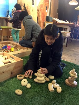 郡上の木を使った積木で遊ぶ子ども。つるつるしたさわり心地で木の温かみを感じられる。後ろには木くずを集めた砂場のような遊び場があり、店内はふんわりと木のいい香りに包まれていた