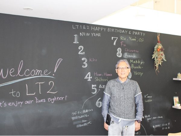 有限会社デクーンの代表・奥村秀喜さん。後ろの黒板は、奥村さんのお気に入りで、入居者同士の連絡事項が書かれることも