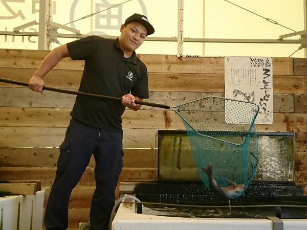 生け簀から生きた魚を掬う、スタッフの三宅松治さん