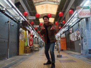 「新世界市場」にてポーズをとる森田純多さん（30歳）。平日午後13時過ぎにもかかわらず、お店は２割弱ほどしか開いていない