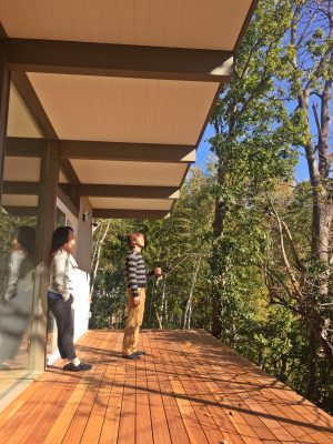 取材にご協力いただいた長崎さん夫婦。<br>
丘の上に建つ家のデッキからは壮観な風景が広がっている。1.8ｍあるという軒は計算しつくされ、冬はリビングまで陽射しを取り込み、夏は遮る設計となっている。ほぼガラス張りになったリビングは、冬の取材時でもとても暖かかった