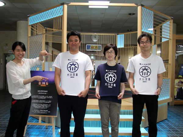 大川市役所に展示されている組み立て式茶室「MUJOAN]の前でPRする大川市職員。普段からおそろいのＴシャツを着て業務にあたっている