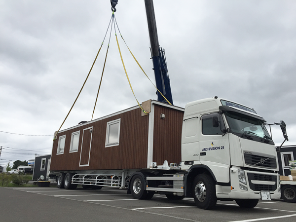 スマートモデューロをクレーンで吊って、海上コンテナ用の輸送トレーラーに載せている様子。スマートモデューロについている箱金物とトレーラーがワンタッチで固定されるという仕組み（提供：アーキビジョン21）