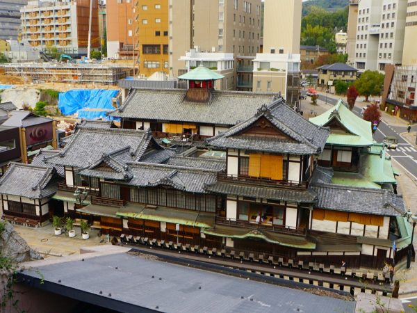 ▲道後温泉本館の中でも一番古い建物は、奥に見えている三階建ての『本館三層楼』。現在改札口がある西向きの玄関棟は昭和に入ってから増築されたもので、改築当時は北側の玄関から出入りしていた（そのためシンボルである振鷺閣の白鷺は北側を向いている）。手前に見えるのが南棟。東側の青銅色の屋根が『又新殿・霊の湯棟』。浴槽の改築のために“家曳き”をしたこともあるという