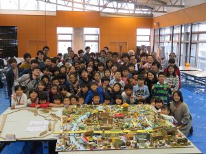 こどもたちに加え、学生、社会人スタッフ、市長や市議会議長などの関係者も集まり、完成した模型を前にした2018年の記念写真。毎回、これだけの人が関わっている