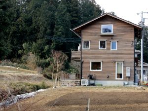 飯能市産の木材「西川材」を使って建てた、移住第一号の家。<br>手前は家庭菜園の予定地で、農業普及員のアドバイスなどを受けて、草取り、整地を行った
