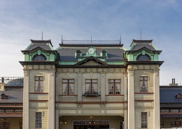 復原された門司港駅。中央の棟は天然石板スレート葺きのマンサード屋根だ。国内では石板スレートを製造しているところが見つからず、カナダから輸入したという。壁面上部の緑色の部分は銅板。年月を経て緑青をふいたためこの色になった。「一方で、新しく1階と2階の間などに使った新しい銅板（茶色く見える部分）が同じように緑になるかどうかは時間が経ってみないと分かりませんね」とＪＲ九州の稲盛さん。中央棟の両端にある柱型（ジャイアントオーダー）が建物に格調を添えている（写真提供：ＪＲ九州）