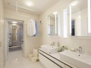 天気や時間を気にせずに洗濯などの家事ができる、慌ただしい時間の身支度にも便利なダブルボウルを設えた機能的な洗面室。奥は浴室で隣にはキッチンとクローゼットがあり、キッチン～洗面室～浴室～クローゼットを集中させることで家事動線を短縮。乾いた洗濯物はすぐ隣にあるクローゼットにしまえる。2本のライン照明を設置したオリジナルのミラーは顔に陰が出にくく、メイクにも重宝する