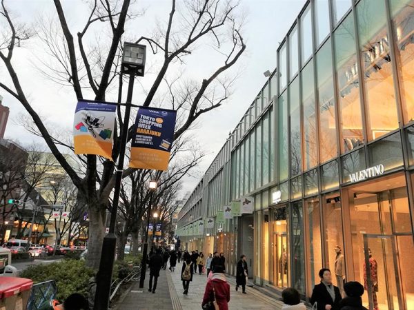 表参道ヒルズなどの店舗が並ぶ参道のなだらかな坂に掲げられたキャンペーンフラッグが風になびく。2019年は、例年実施されている「スクラッチキャンペーン」の当たり本数を⼤幅に追加。500円当たり券を新規投⼊し、当たり本数合計1万2,040本（昨年度4,030本の約3倍）としてパワーアップした。2⽉1～14⽇の“コアウィーク”には、表参道に「インフォメーション用テント」を設営し、英語・中国語が話せるコンシェルジュがキャンペーンを案内。さらに「⾦屏⾵パネル」を置き、フォトスポットとしても機能していた