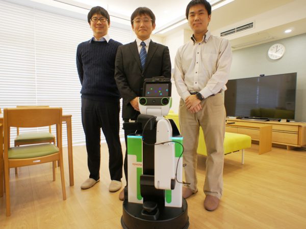 ロボティックスマートホーム実証研究施設の田辺茂雄氏（中央）とスタッフのお二人</br>手前は、頼れるヒューマンサポートロボットの「トヨちゃん」