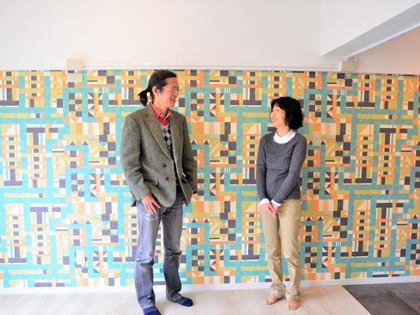 円谷さん夫婦お気に入りの壁紙の前で（１階）。「竹久夢二の壁紙セレクション」の中の１枚。「真っ白な壁だときれいではありますが、インパクトを取りました（笑）」