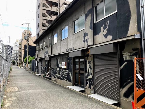 線路沿いの道路に面した「鶴身印刷所」。壁画は、ポートレイトペインター・山本勇気さんによるもの。手前の大きな顔は元工場長。電車の進行方向に沿って歴史が展開するストーリーで、かつての印刷所の様子が描かれている