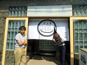 おふろ荘の入り口で。左が話を伺った和泉直人氏、右はインターンの頃から関わってきた中村実穂氏