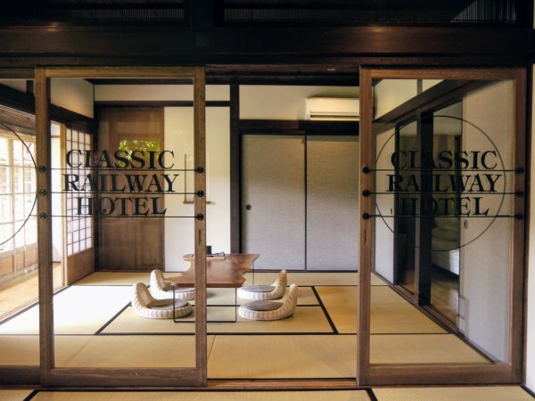 「クラシックレールウェイホテル人吉球磨」の畳のリビング。昔ながらの縁側のある和室の雰囲気はそのままに、襖をガラスの建具に入れ替えた。アイアン作家が製作したロゴをあしらっている