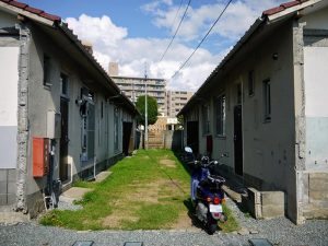 オビハウス外観。芝を張った中庭を挟んで長屋が向かい合う。左を母屋、右を離れとし、母屋には中庭の反対側に玄関を設けた