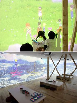 プレイルームのスクリーンに投映された「分身」を見て楽しむ子ども（上）。絵に色を塗って「分身」を準備するための机が並ぶ（下）