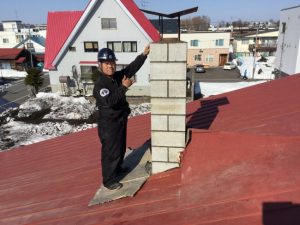 倒れた集合煙突を修復する横山さん。素焼きの土管と鉄筋、ブロックを一段ずつ組み上げて完成させる