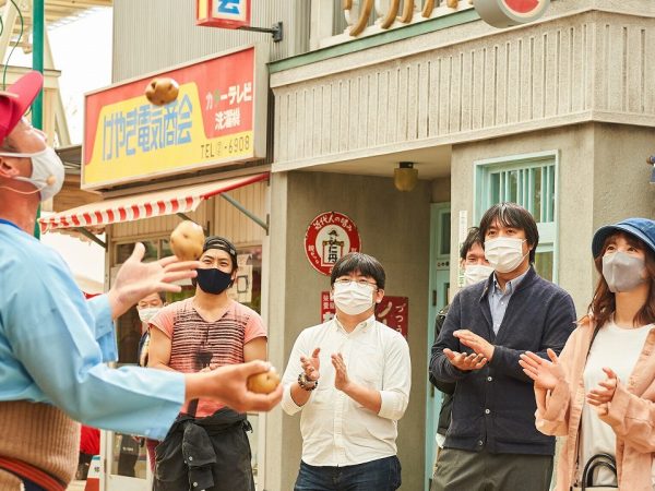 ▲昭和のドラマに出てきそうな典型的な“駐在さんと盗人”のパフォーマンス。商店街のお店や店主・住人達にはあらかじめ名前やキャラクターが設定されており、お節介でお人好しで人情味あふれる住人たちとのリアルな掛け合いが来場客を和ませる。こうした大小のパフォーマンスは一日に数回行われているが、臨場感を大切にするためあえて開催時間を予告していない。「お客様の様子を見ながら、住人たちが口上や絡みの内容を毎回変えています（広報担当者談）」