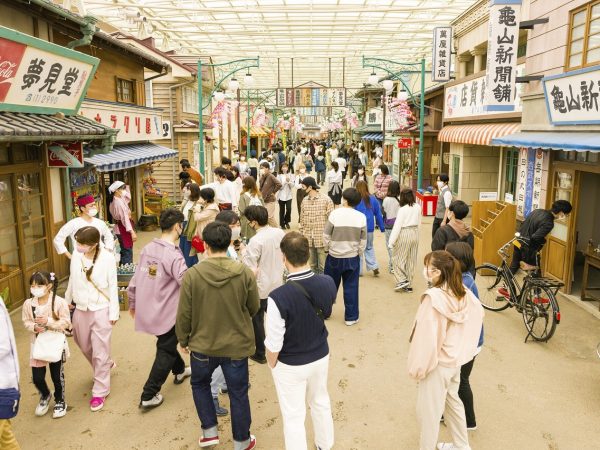 ▲園内へ足を踏み入れると、最初に広がるゾーンが1960年代の商店街の街並みをイメージした『夕日の丘商店街』だ。商店街の全長は約150ｍ。30店舗のうち15店舗は飲食や物販など体験型の実店舗。残る15店舗はパフォーマンスのステージや写真撮影ができるセットになっている。商店街の建物意匠については時代考証を重ね、当時の建築様式・生活様式を再現。厳密には1960年代の建物ではなく大正から昭和初期にかけてのレトロな建物となっているため、ホーロー看板など小道具の中にはすでに手に入らないアイテムも多く、わざわざ新たに製作したものも含まれている