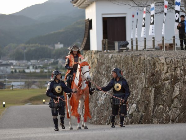 ▲『大洲城キャッスルステイ』では、大洲城天守と重要文化財のふたつの櫓を貸し切りにして宿泊できる。別の場所でチェックインを終えたあと、衣装を着替え「入城セレモニー」を体験するところからキャッスルステイがスタートする。城主（男性）は甲冑姿、姫（女性）は着物姿で家来を引き連れて入城※子ども用衣装もある。これは江戸初期1617年の加藤貞泰入城のシーンを再現したものだ