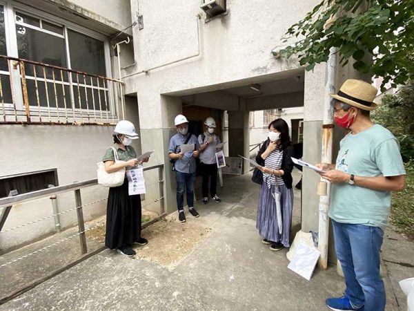 「旧魚の町団地」の見学会で、参加者に解説する安武敦子長崎大学教授（右から2人目）。階段室前はピロティのようになっている。上部は後年に増設した浴室（詳細は後述）