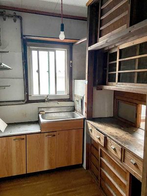 台所には床から天井までの棚が造り付けられている。引き出しや引き違い、網入りの戸など、きめ細かな設計だ。棚の右奥には配膳のためのハッチが見える。流し台は更新されているが、シンクの隣にダストシュートが残る