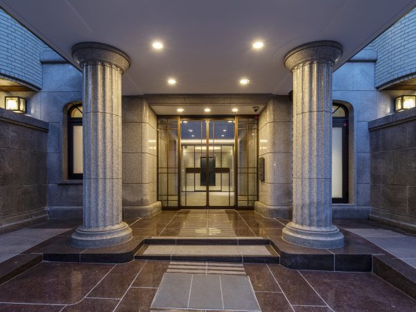 石と取り合う袖枠は既存を生かし、開き部だけオートドアに改修。雨どいも同色に再塗装して再生している