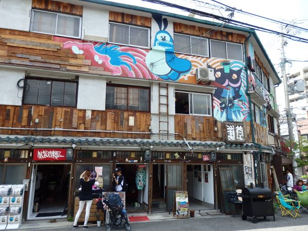 大阪・浪速にある築60年の木造3階建ての文化住宅をリノベーションし、地域の人々やアーティストを巻き込み人が自然に集う場所に。休日になると1階部分が街に向かって開かれ、大家さんで元料理人の田中さんが料理も提供している。