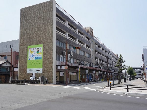 「emCAMPUS」東棟。1階にはフードホールとショップ、2・3階に市立図書館、4・5階にはオフィスや市役所の市民課窓口など行政機関、大学のサテライトオフィスなど、6～24階は分譲マンション、低層棟の屋上にはマンション居住者向け共有スペースとして農園を整備した。右側の工事中のところが西棟になる。また、「emCAMPUS」と駅前大通を挟んだ北側、2020年に閉店した「ほの国百貨店」の跡地も再開発でマンションなどが入る大規模施設を予定した工事が進行中