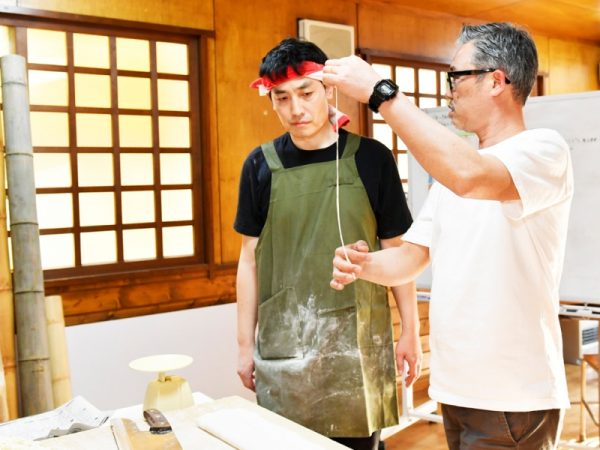 佐野らーめんの伝統技法「青竹打ち」の指導を受ける研修生