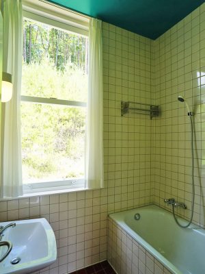 ▲ターコイズブルーの天井がお洒落なバスルーム。天井高いっぱいの大きな窓から緑を眺めることができる。スイッチ、コンセント等のパーツをよりリアルに再現するため、邸内ではデンマークと同じ200ボルトを採用している