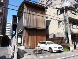 公道から建物を見たところ。格子の壁の裏にコンテナ、長屋がある。格子は周囲に合わせるためのデザイン