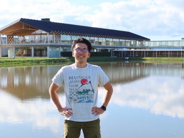 スイデンテラスを背景に長岡氏。来ているTシャツは自らデザインして作ったもの