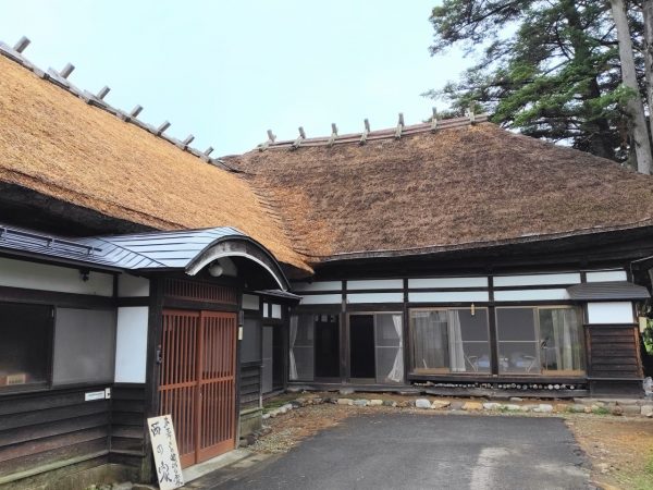 存在感のある茅葺屋根が特徴の「茅葺の曲がり家 西の家」の外観。手前が納屋で奥に母屋がある