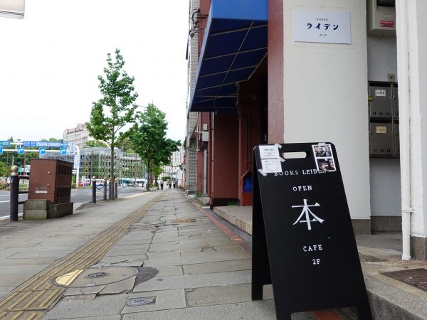 大通り沿いの歩道に置かれた「本」の立て看板。右奥の階段から店へ