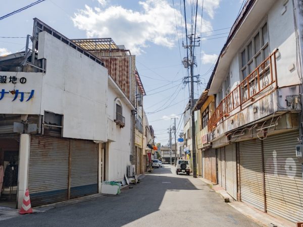 港町商店街の様子。手前は茶舗「樋口芳泉園茶舗」。中央の茶色いモダンな建築は銭湯「みなと湯」だったが、現在は廃業。奧は玉島の鎮守・羽黒神社の東参道口