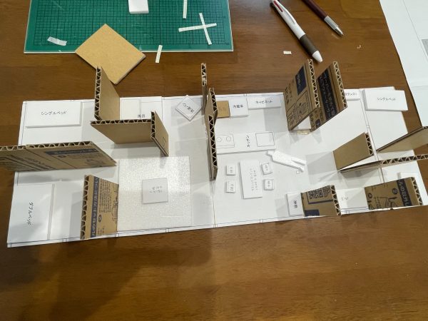 家族揃って話し合いながら、模型の壁や家具などを動かして間取りを検討していく。VUILDの一級建築士、中西朱理さん（写真中央）も同席してアドバイスした。３月以降、家族はみなし仮設住宅で暮らしている（写真／介川亜紀）　