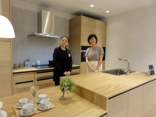 クリナップ・キッチンタウン・東京のキッチンと同素材のテーブルがプランできる「CENTRO」の展示を前に、使い勝手を説明する熊谷香さん（左）と小泉恭子さん(右)